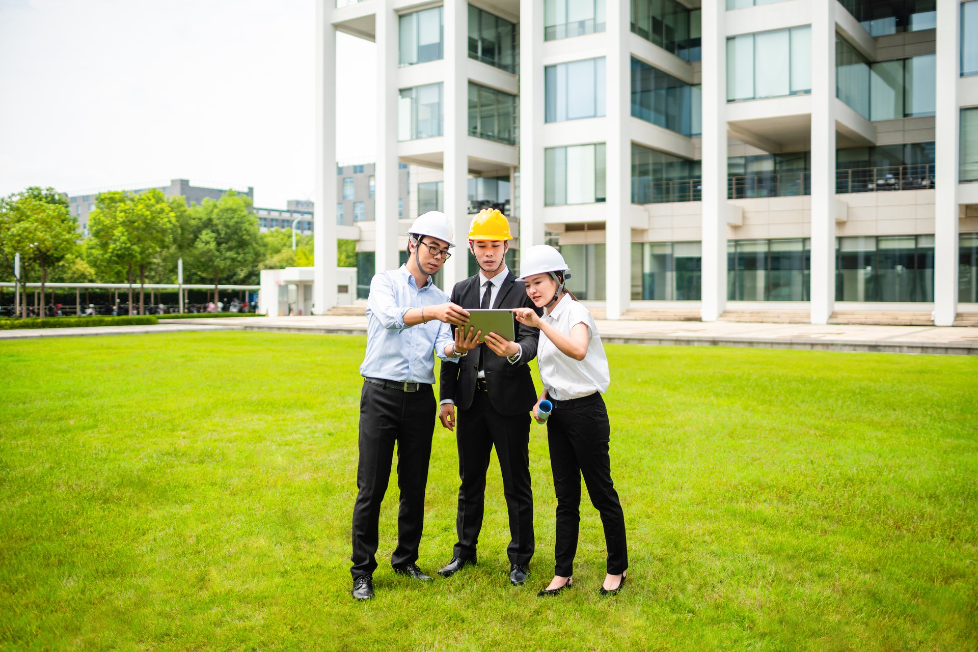 Three business people looking at the tablet on the grass